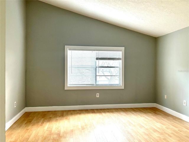 empty room featuring lofted ceiling, light hardwood / wood-style floors, and a textured ceiling