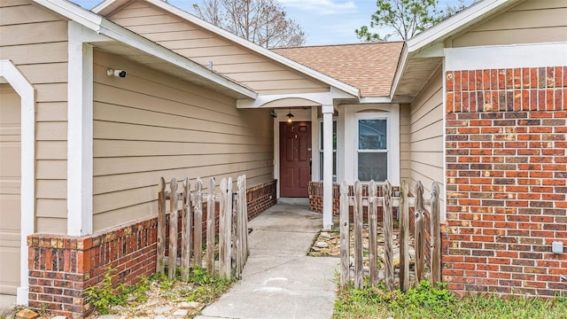 doorway to property featuring roof with shingles, fence, and brick siding