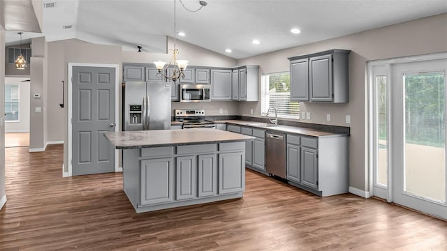 kitchen featuring gray cabinetry, stainless steel appliances, a sink, hanging light fixtures, and a center island