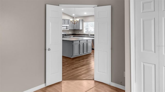 kitchen featuring light wood-style floors, appliances with stainless steel finishes, gray cabinets, and a chandelier