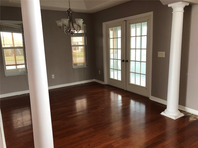 unfurnished dining area featuring french doors, a notable chandelier, dark hardwood / wood-style flooring, and ornate columns