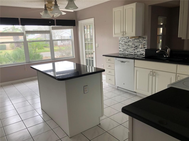 kitchen with light tile patterned flooring, a kitchen island, sink, white cabinets, and white dishwasher