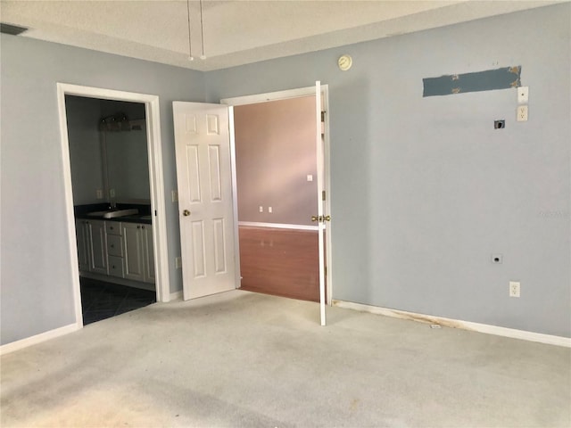 unfurnished bedroom featuring ensuite bathroom, sink, and carpet floors