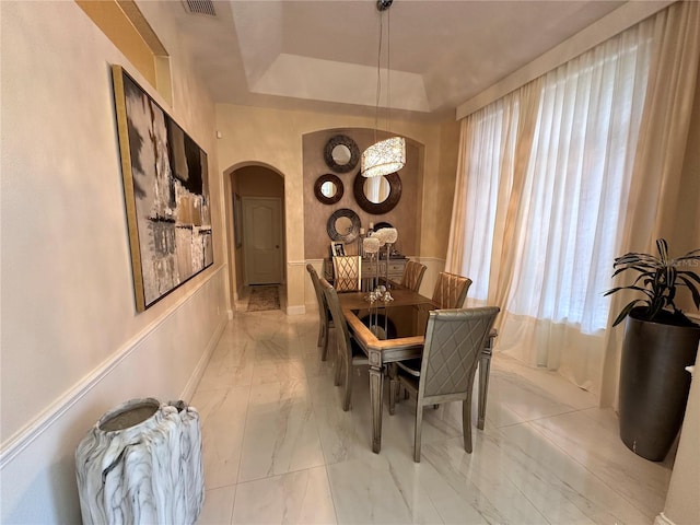 dining area with arched walkways, marble finish floor, a raised ceiling, and baseboards