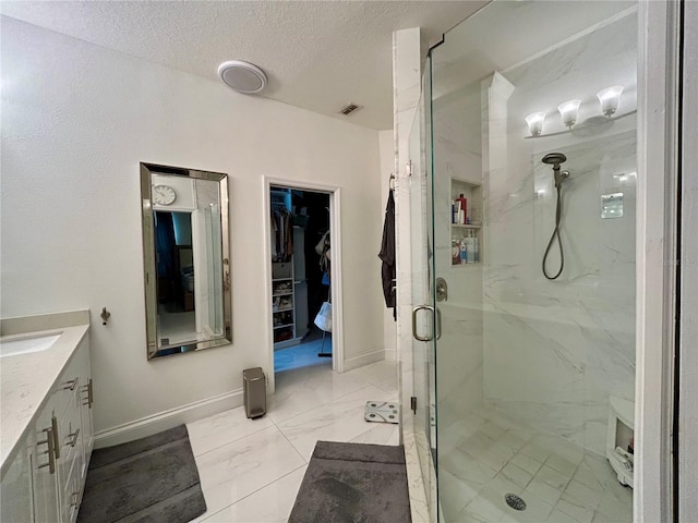 full bath with a marble finish shower, marble finish floor, a walk in closet, a textured ceiling, and vanity