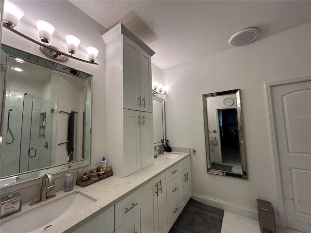 bathroom with double vanity, a stall shower, a textured ceiling, and a sink