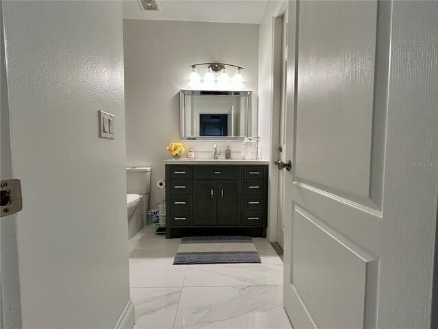 half bath featuring marble finish floor, vanity, and toilet