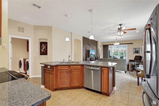 kitchen featuring a center island with sink, stainless steel appliances, washing machine and clothes dryer, sink, and pendant lighting