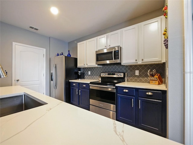 kitchen featuring stainless steel appliances, blue cabinetry, white cabinets, and backsplash