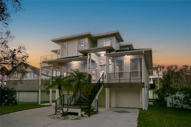 view of front of home with an attached garage, a balcony, stairs, concrete driveway, and a lawn