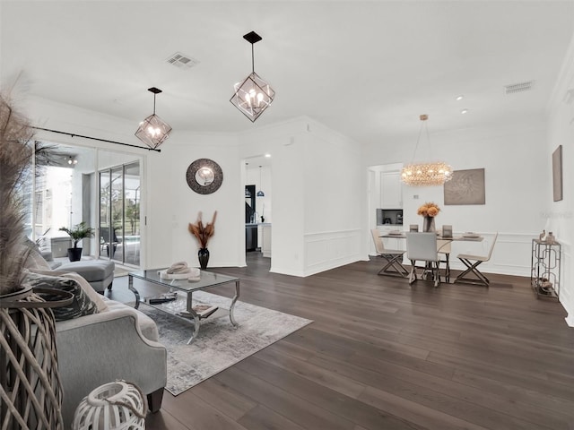 living area with an inviting chandelier, visible vents, a decorative wall, and dark wood-type flooring