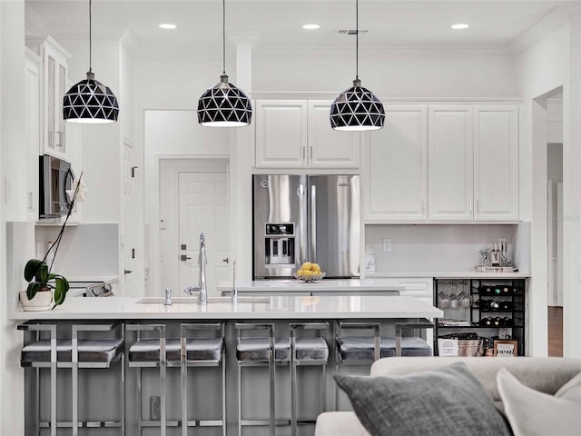 kitchen featuring a breakfast bar area, stainless steel appliances, hanging light fixtures, white cabinets, and a sink