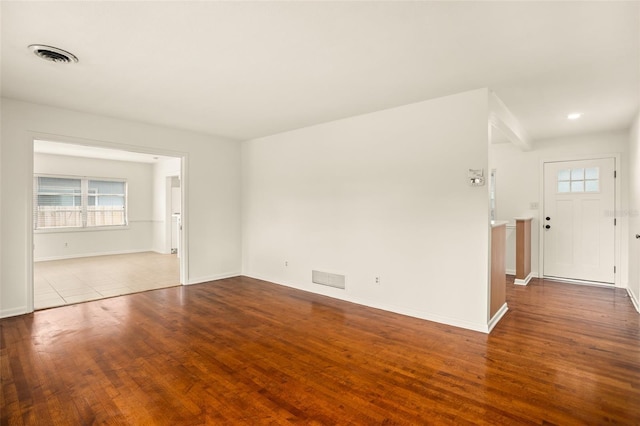 empty room featuring a wealth of natural light, visible vents, and wood finished floors