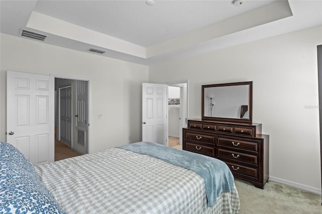 bedroom featuring light colored carpet, a tray ceiling, and a walk in closet