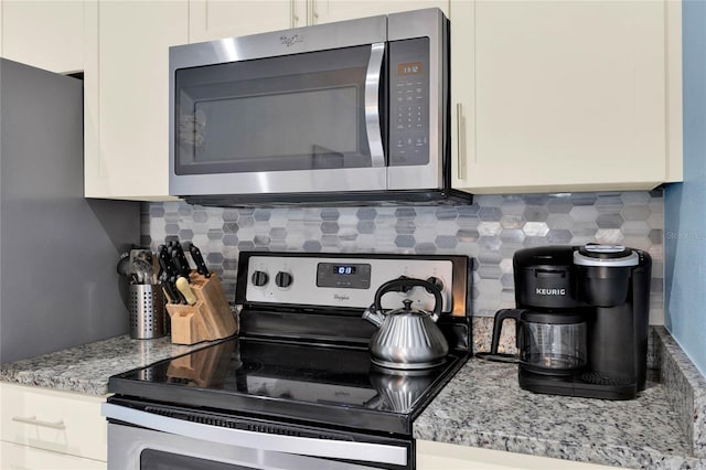 kitchen with tasteful backsplash, light stone countertops, white cabinets, and appliances with stainless steel finishes