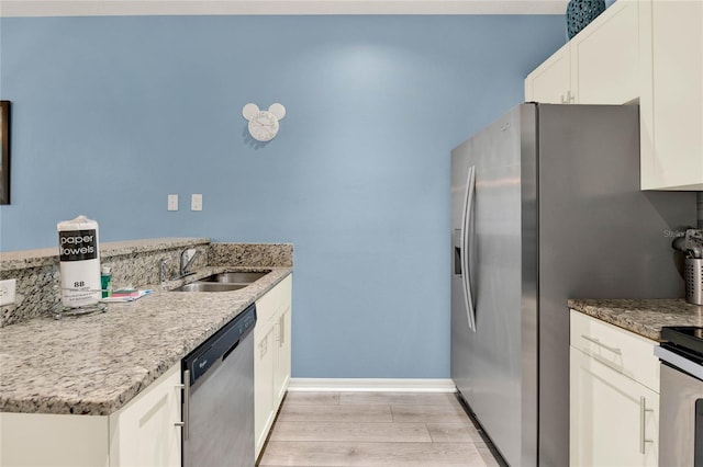 kitchen with white cabinetry, sink, light stone counters, light hardwood / wood-style floors, and stainless steel appliances