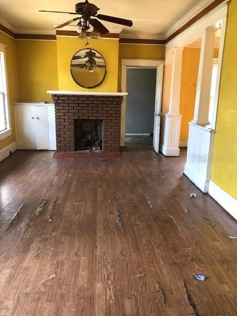 unfurnished living room with a brick fireplace, crown molding, baseboards, and wood finished floors