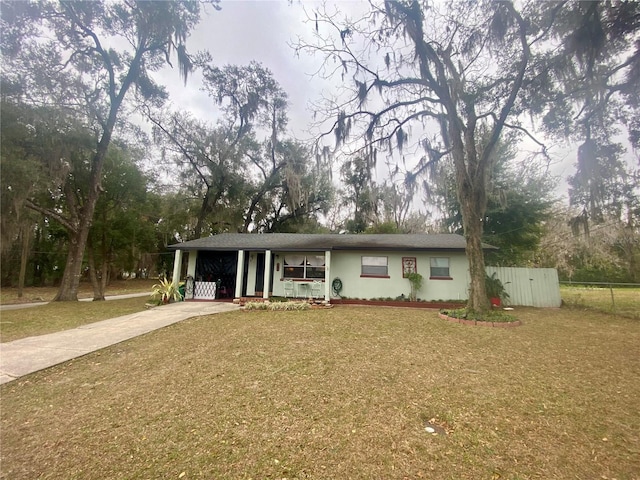 ranch-style house featuring concrete driveway, stucco siding, covered porch, fence, and a front yard