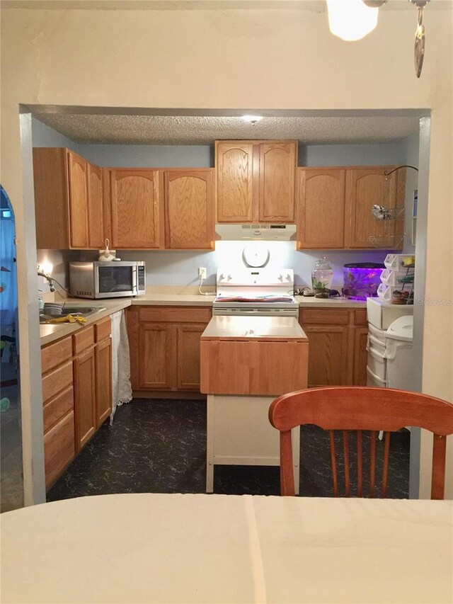 kitchen with a sink, stainless steel microwave, light countertops, under cabinet range hood, and white range with electric cooktop