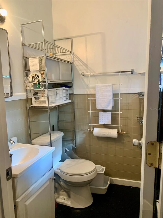bathroom with tile walls, toilet, vanity, and a wainscoted wall
