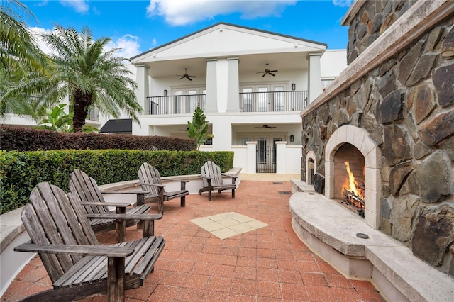 back of house featuring ceiling fan, a balcony, a patio area, and an outdoor stone fireplace