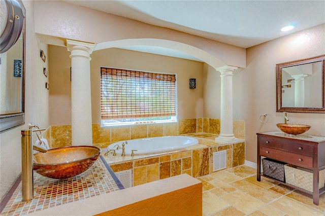 bathroom featuring ornate columns, vanity, and tiled bath