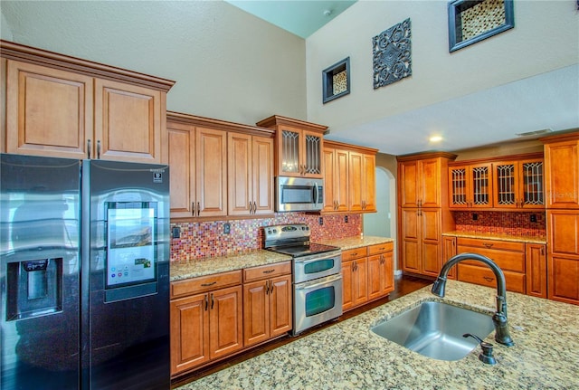 kitchen with light stone counters, sink, decorative backsplash, and stainless steel appliances