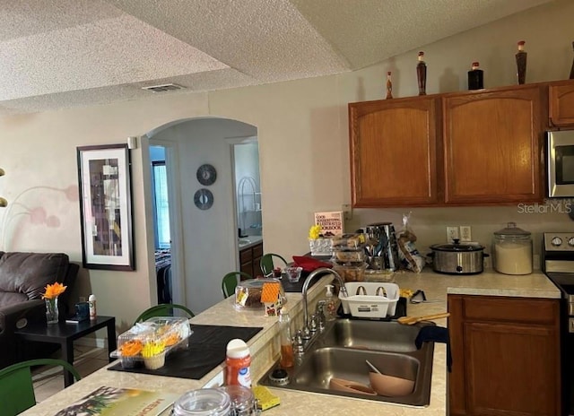 kitchen featuring vaulted ceiling, appliances with stainless steel finishes, sink, and a textured ceiling