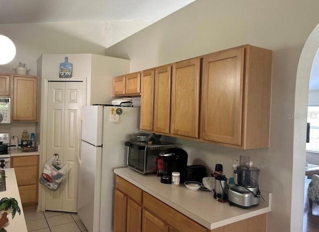 kitchen featuring stove, vaulted ceiling, light tile patterned flooring, and white fridge