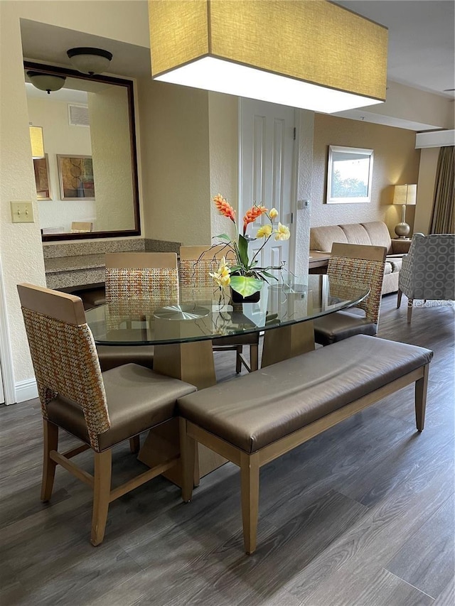 dining space featuring a textured wall, wood finished floors, visible vents, and baseboards