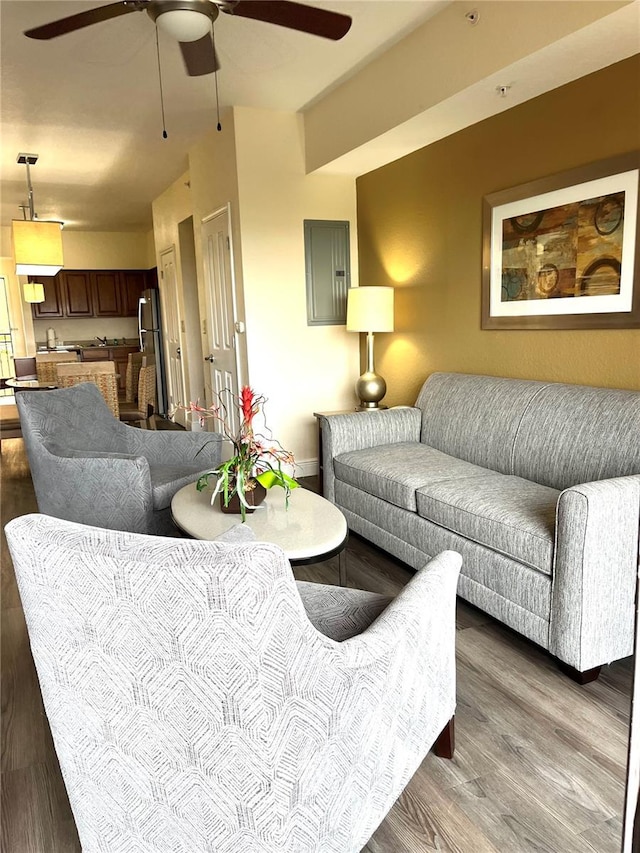 living area with baseboards, electric panel, a ceiling fan, and wood finished floors