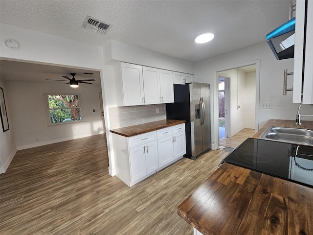 kitchen featuring sink, butcher block counters, light hardwood / wood-style floors, white cabinets, and stainless steel fridge with ice dispenser