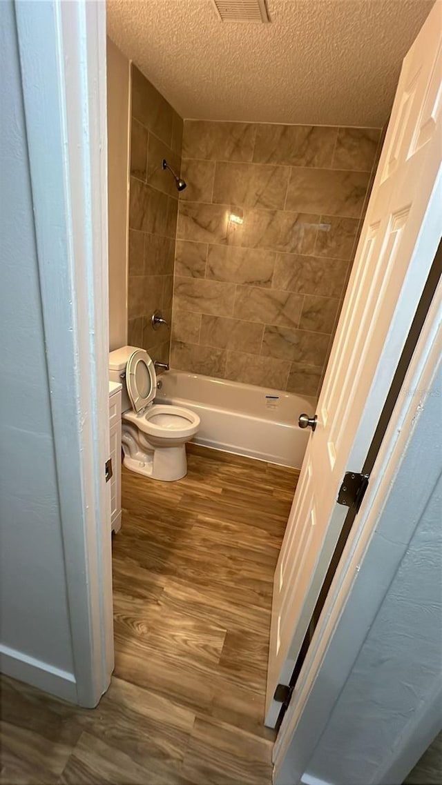 full bathroom with tiled shower / bath, hardwood / wood-style flooring, vanity, toilet, and a textured ceiling