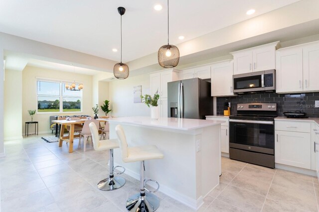 kitchen featuring a kitchen island, appliances with stainless steel finishes, white cabinets, decorative backsplash, and hanging light fixtures