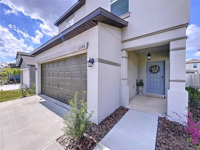 view of exterior entry featuring a garage, concrete driveway, and stucco siding