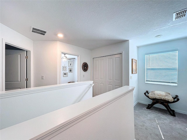 hallway with a textured ceiling, carpet floors, and visible vents