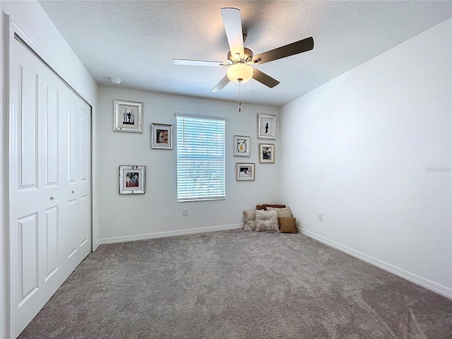 unfurnished bedroom with a closet, dark carpet, a ceiling fan, a textured ceiling, and baseboards