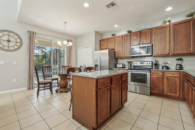 kitchen featuring appliances with stainless steel finishes, a kitchen island, light stone counters, and decorative light fixtures