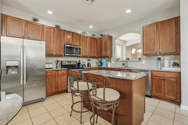 kitchen featuring a breakfast bar, sink, light stone counters, a kitchen island, and stainless steel appliances