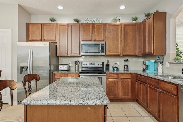 kitchen featuring a center island, appliances with stainless steel finishes, light stone countertops, and backsplash