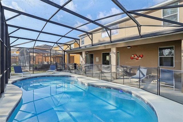 view of swimming pool with glass enclosure, ceiling fan, and a patio area