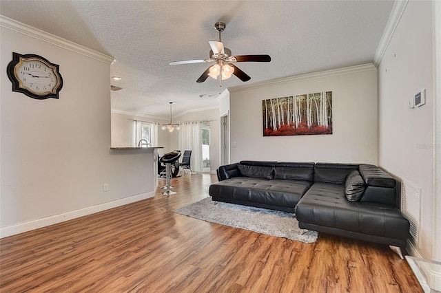 living room with ceiling fan with notable chandelier, ornamental molding, a textured ceiling, and light wood-type flooring