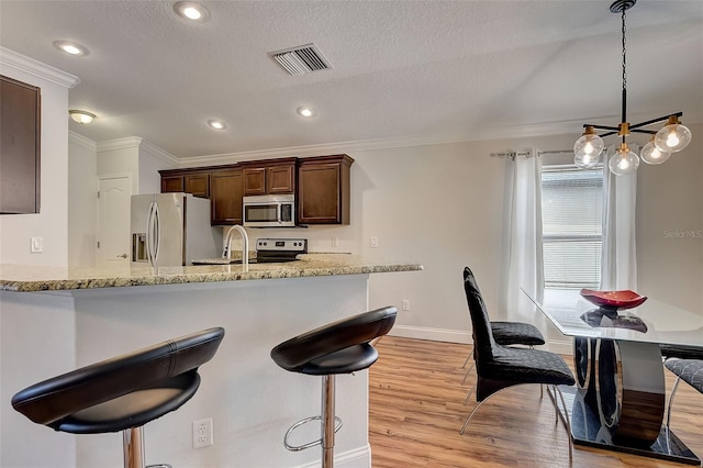 kitchen featuring appliances with stainless steel finishes, hanging light fixtures, light stone counters, dark brown cabinets, and light hardwood / wood-style flooring