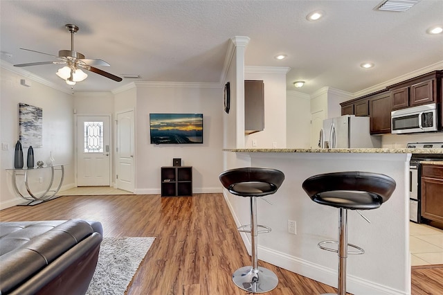 kitchen with light stone counters, crown molding, appliances with stainless steel finishes, a kitchen breakfast bar, and light hardwood / wood-style floors