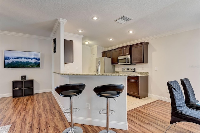 kitchen with dark brown cabinetry, light hardwood / wood-style flooring, ornamental molding, and appliances with stainless steel finishes