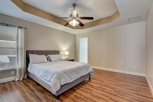 bedroom featuring hardwood / wood-style floors, a raised ceiling, and ceiling fan