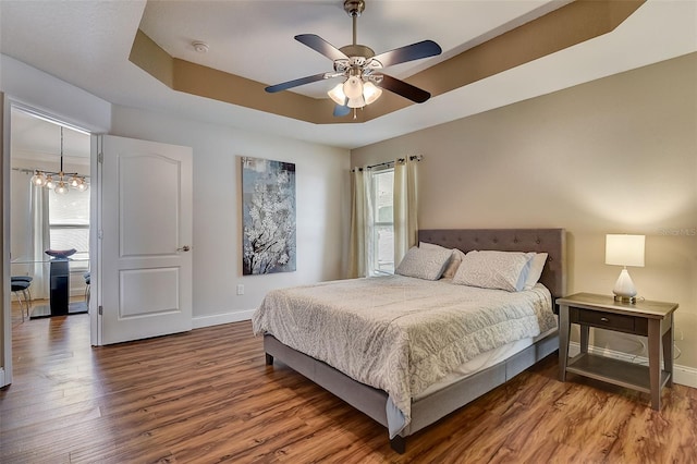 bedroom with hardwood / wood-style flooring, a tray ceiling, and ceiling fan with notable chandelier