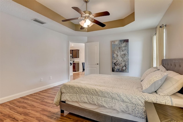 bedroom featuring hardwood / wood-style flooring, a raised ceiling, and ceiling fan