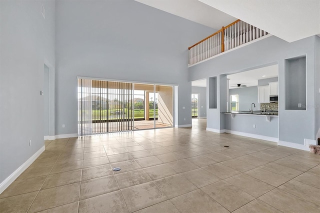 unfurnished living room featuring light tile patterned flooring, a sink, and baseboards