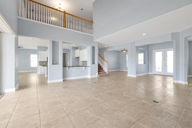 unfurnished living room with baseboards, french doors, stairway, and a healthy amount of sunlight